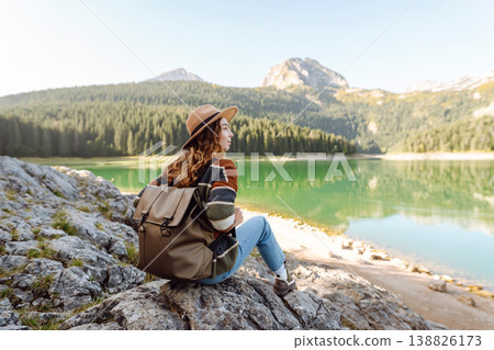 Young woman traveler enjoys fresh air and a beautiful view of the lake and mountains. Active life Young woman traveler enjoys fresh air and a beautiful view of the lake and mountains. Active life 138826173