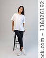 Casual Asian content creator dressed in white shirt relaxing on stool for social media visuals 138826192