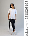Casual Asian content creator dressed in white shirt relaxing on stool for social media visuals 138826198