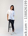 Casual Asian content creator dressed in white shirt relaxing on stool for social media visuals 138826199