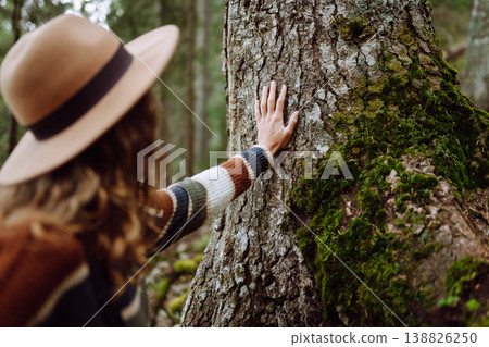 Female tourist with backpack and travel equipment touching tree while standing in the forest. Female tourist with backpack and travel equipment touching tree while standing in the forest. 138826250