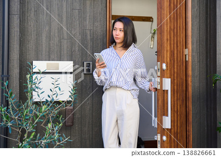 A Japanese woman leaves the front door of a detached house, smartphone in hand. A Japanese woman leaves the front door of a detached house, smartphone in hand. 138826661
