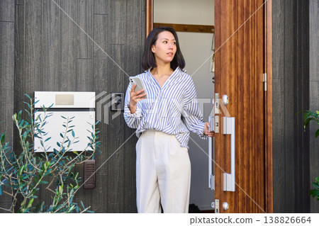 一位日本女子手持智慧型手機,走出獨棟房屋的前門。 一位日本女子手持智慧型手機,走出獨棟房屋的前門。 138826664