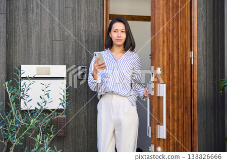 A Japanese woman leaves the front door of a detached house, smartphone in hand. A Japanese woman leaves the front door of a detached house, smartphone in hand. 138826666