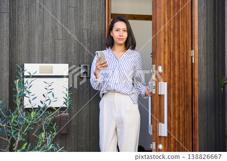 一位日本女子手持智慧型手機,走出獨棟房屋的前門。 一位日本女子手持智慧型手機,走出獨棟房屋的前門。 138826667