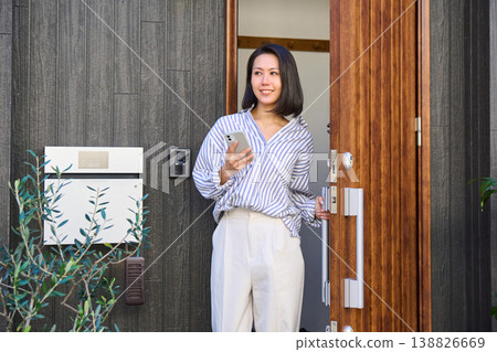 A Japanese woman leaves the front door of a detached house, smartphone in hand. A Japanese woman leaves the front door of a detached house, smartphone in hand. 138826669