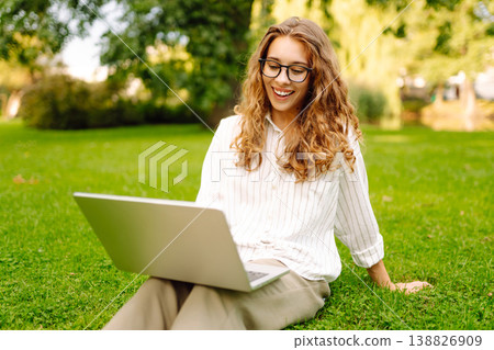 Happy Woman with laptop sit green grass at park. Studying outdoors. Freelancing concept 138826909