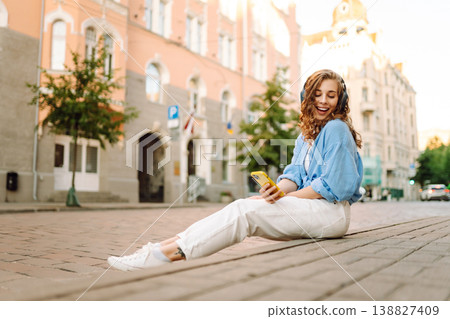 Happy relaxed woman in wireless headphones choosing, listening favorite music in urban city street. 138827409