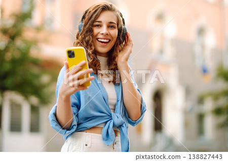 Happy relaxed woman in wireless headphones choosing, listening favorite music in urban city street. 138827443