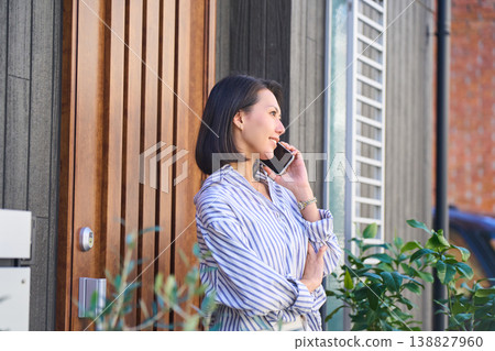 A Japanese woman's profile as she makes a phone call in front of her house. 138827960