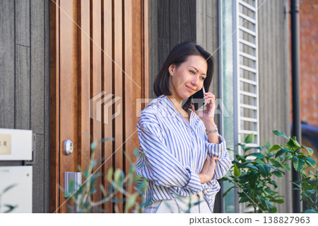 A Japanese woman's profile as she makes a phone call in front of her house. 138827963