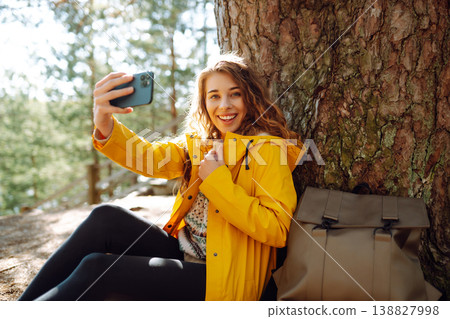 Happy woman with phone in hands taking selfie in forest. Young tourist enjoying spring day near lake 138827998