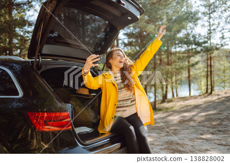Happy Woman is resting in trunk of car and taking selfie. Travel, tourism, nature, active life. Happy Woman is resting in trunk of car and taking selfie. Travel, tourism, nature, active life. 138828002