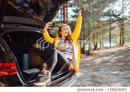 Happy Woman is resting in trunk of car and taking selfie. Travel, tourism, nature, active life. Happy Woman is resting in trunk of car and taking selfie. Travel, tourism, nature, active life. 138828003