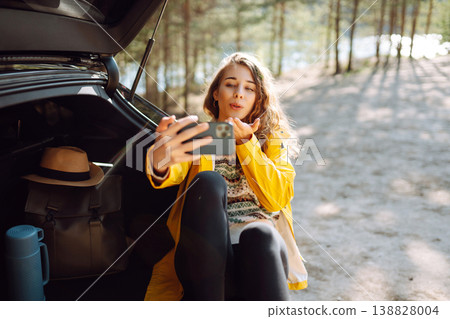 Happy Woman is resting in trunk of car and taking selfie. Travel, tourism, nature, active life. Happy Woman is resting in trunk of car and taking selfie. Travel, tourism, nature, active life. 138828004