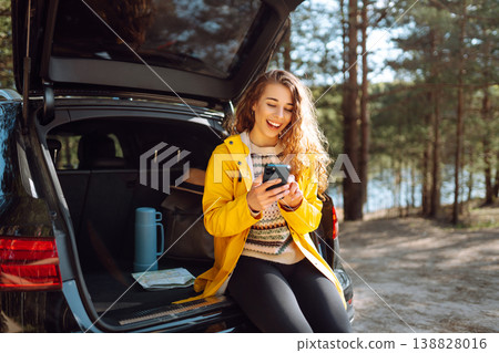 Young woman sitting in open trunk with phone. Lifestyle, travel, tourism, nature, active life. 138828016
