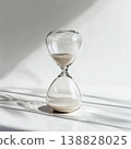 Transparent Glass Hourglass on White Background with Sunlit Minimalist Composition 138828025