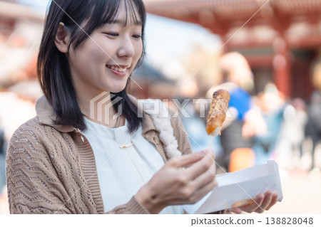 一位女士手拿團子（米糰子），面帶微笑；在旅遊景點邊走邊吃；日本甜點；假期。 138828048