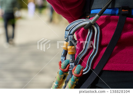 Close up of metal carabiners and ropes attached to safety harness on person in adventure park Close up of metal carabiners and ropes attached to safety harness on person in adventure park 138828104