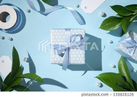 Elegant blue gift box with ribbon bow, pearls and green leaves on pastel background. Elegant blue gift box with ribbon bow, pearls and green leaves on pastel background. 138828126