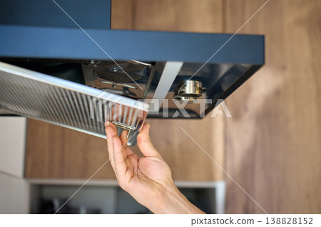 Hand removing a metal filter from a modern kitchen hood Hand removing a metal filter from a modern kitchen hood 138828152