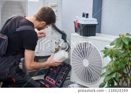 Technician servicing outdoor heat pump unit at residential house Technician servicing outdoor heat pump unit at residential house 138828169