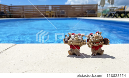 A Shisa statue relaxing by the poolside, against a blue sky and a resort summer scene. Awamori (Okinawan liquor). Okinawa Prefecture. A Shisa statue relaxing by the poolside, against a blue sky and a resort summer scene. Awamori (Okinawan liquor). Okinawa Prefecture. 138828554