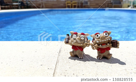 A Shisa statue relaxing by the poolside, against a blue sky and a resort summer scene. Awamori (Okinawan liquor). Okinawa Prefecture. A Shisa statue relaxing by the poolside, against a blue sky and a resort summer scene. Awamori (Okinawan liquor). Okinawa Prefecture. 138828555