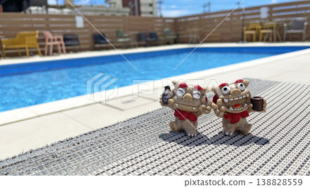 A Shisa statue relaxing by the poolside, against a blue sky and a resort summer scene. Awamori (Okinawan liquor). Okinawa Prefecture. 138828559