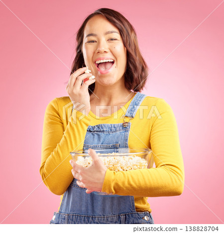 Portrait, asian woman and eating popcorn in studio while watching movie, film or cinema show on pink background. Happy female model, bowl or snack to enjoy streaming, subscription or tv entertainment 138828704