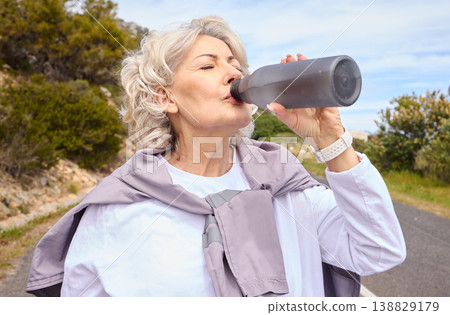 Elderly woman, drinking water and bottle on road for fitness, running or thinking for vision, hydration or health. Mature lady, runner and detox with relax for wellness, exercise or workout in nature 138829179
