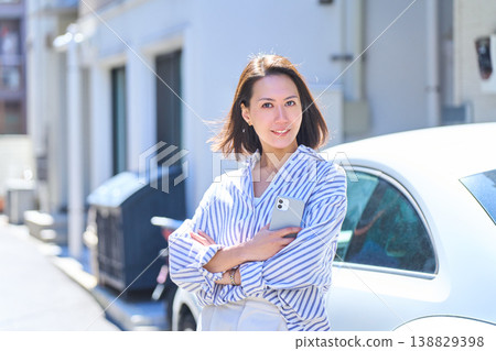 A portrait of a Japanese woman smiling and holding her smartphone outdoors in the sunshine. A portrait of a Japanese woman smiling and holding her smartphone outdoors in the sunshine. 138829398