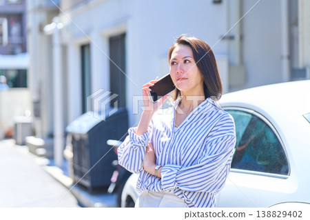 A portrait of a Japanese woman gazing into the distance while talking on her smartphone outdoors. A portrait of a Japanese woman gazing into the distance while talking on her smartphone outdoors. 138829402