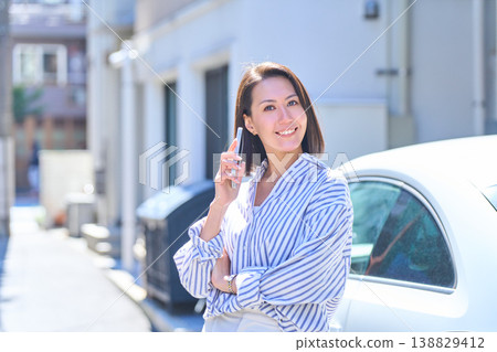 A portrait of a Japanese woman smiling outdoors while holding a smartphone. 138829412