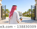 Arab male student walking toward university campus holding books in sunny day 138830309