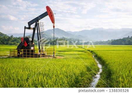 Oil drilling pumpjack in lush rice field landscape with mountains and blue sky Oil drilling pumpjack in lush rice field landscape with mountains and blue sky 138830326