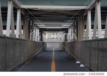 Framed by a symmetrical array of weathered white trusses, this industrial pedestrian overpass stretches forward in a clean, linear perspective. Framed by a symmetrical array of weathered white trusses, this industrial pedestrian overpass stretches forward in a clean, linear perspective. 138830692
