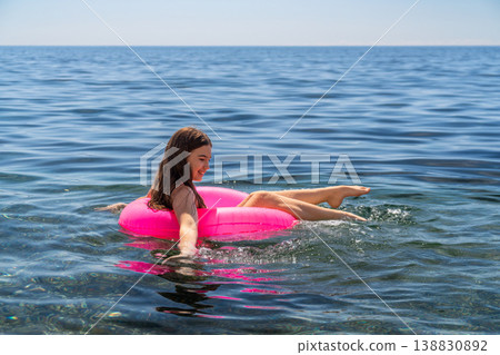 Floating girl pink inner tube, enjoying summer vacation in blue ocean water under clear sky 138830892