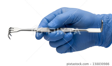 Blue-gloved hand holding a stainless steel double-ended senn retractor with one blunt and one sharp prong, representing surgical exposure and tissue retraction 138830986
