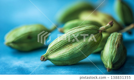 Close-up macro view of vibrant green cardamom pods on a textured blue surface Close-up macro view of vibrant green cardamom pods on a textured blue surface 138831355