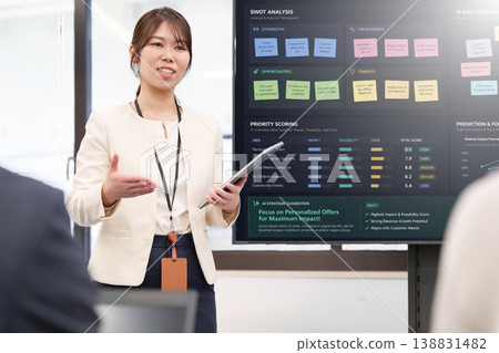 A female employee giving a presentation in front of a large monitor. A female employee giving a presentation in front of a large monitor. 138831482