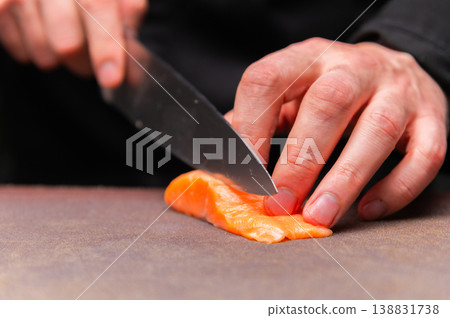 Chef slicing fresh salmon fillet on wooden cutting board with knife Chef slicing fresh salmon fillet on wooden cutting board with knife 138831738