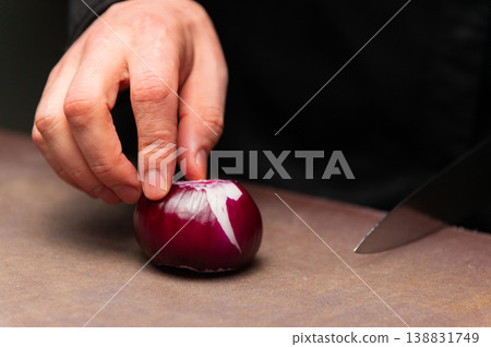 Hand holding red onion on wooden cutting board with knife nearby 138831749