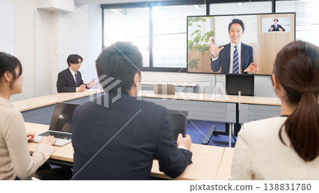 Company employees gather around a large monitor to receive training in a hybrid format. 138831780