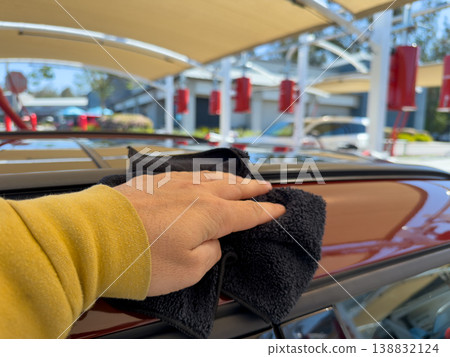 Man wiping and drying car with grey microfiber rag outdoors, closeup 138832124