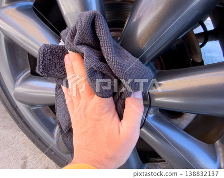 Man wiping and drying car with grey microfiber rag outdoors, closeup 138832137