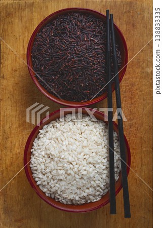 Two clay bowls, of black and white rice, with chopsticks, placed on a wooden surface, no people Two clay bowls, of black and white rice, with chopsticks, placed on a wooden surface, no people 138833335