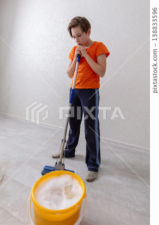 Young child engaged in floor cleaning with a mop and bucket in a cozy indoor space Young child engaged in floor cleaning with a mop and bucket in a cozy indoor space 138833596