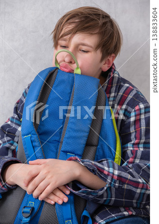 A schoolboy hugs his cold backpack with annoyance and grimaces. A schoolboy hugs his cold backpack with annoyance and grimaces. 138833604