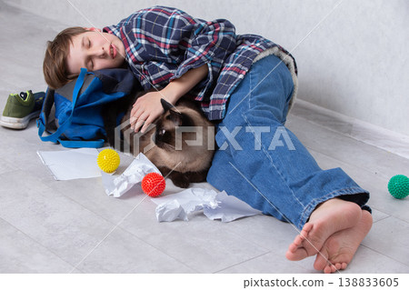 Young boy lies on the floor resting with a cat surrounded by colorful toys and crumpled paper in a cozy indoor setting Young boy lies on the floor resting with a cat surrounded by colorful toys and crumpled paper in a cozy indoor setting 138833605